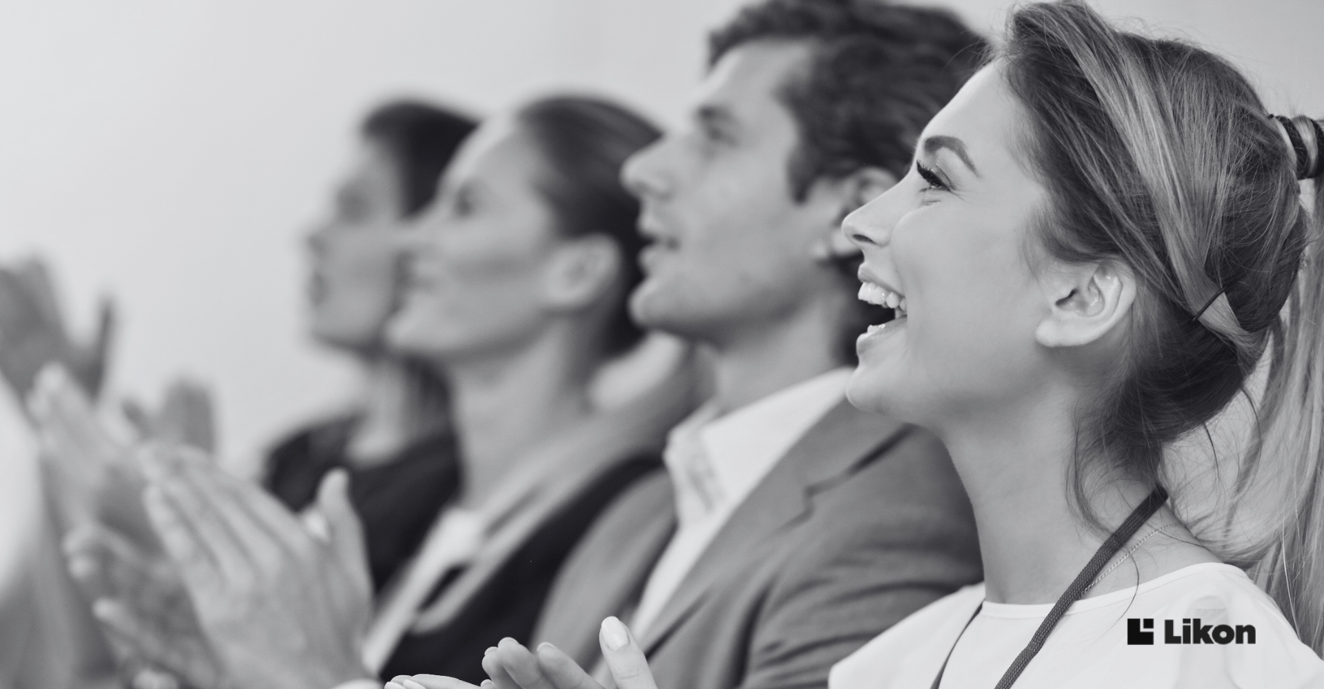 Uczestnicy konferencji siedzą w rzędzie i biją brawo, reagując z entuzjazmem na wystąpienie.