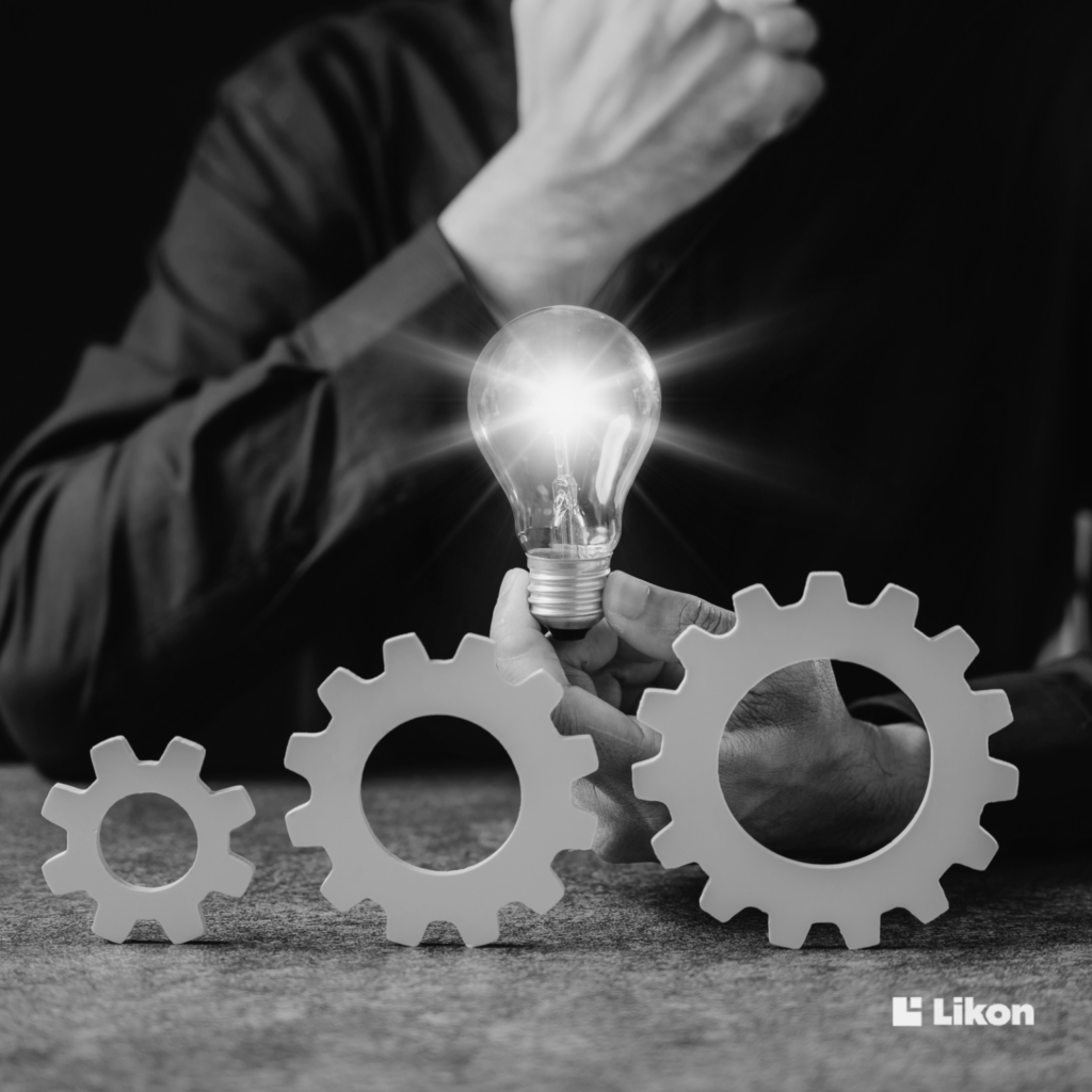Dłoń trzyma świecącą żarówkę nad trzema kołami zębatymi, symbolizującą pomysł i automatyzację procesów w firmie.