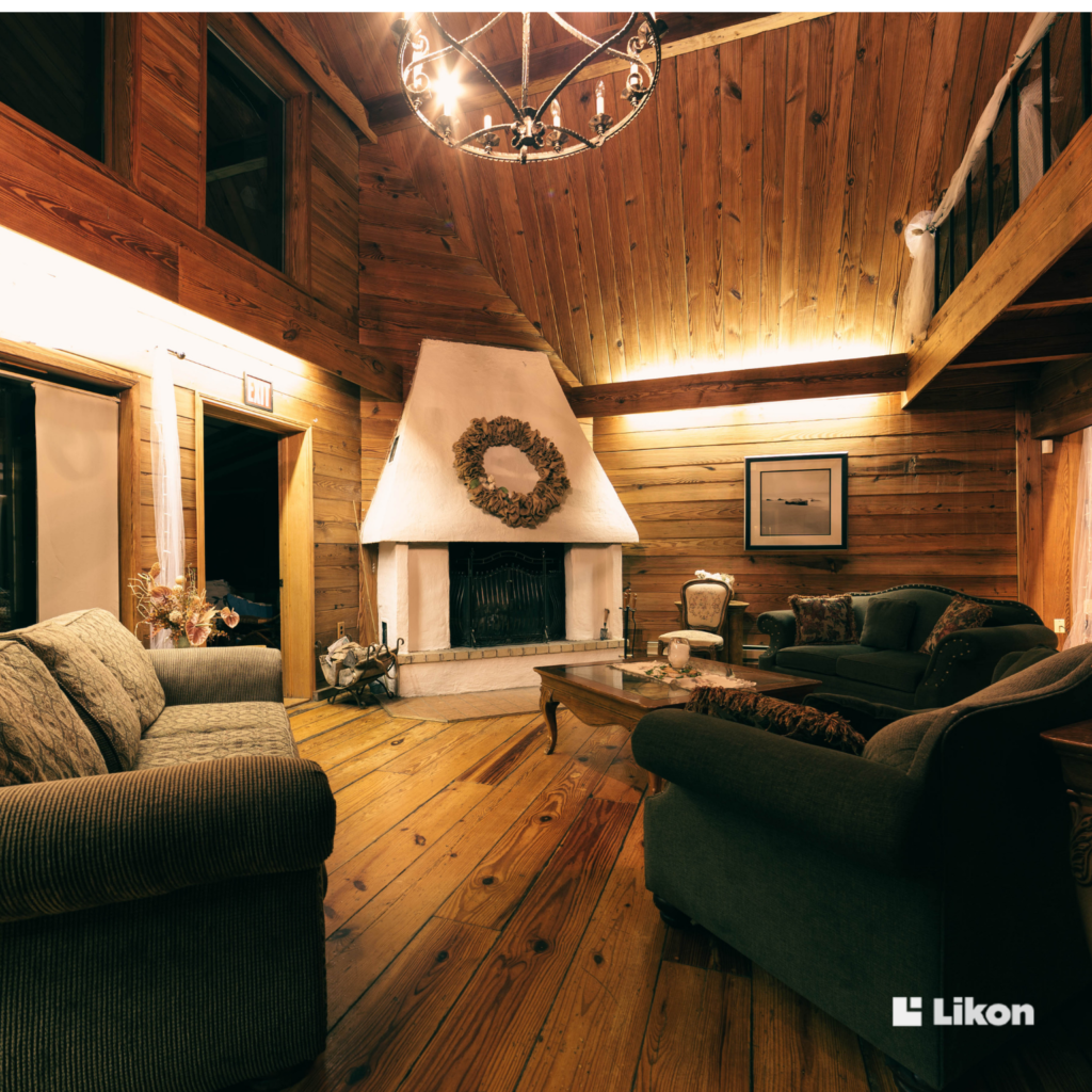 Przytulny salon w drewnianej rezydencji z kominkiem, sofami i ciepłym oświetleniem, pokazujący komfort i sterowanie temperaturą w rezydencji dopasowane do domowej strefy wypoczynku.