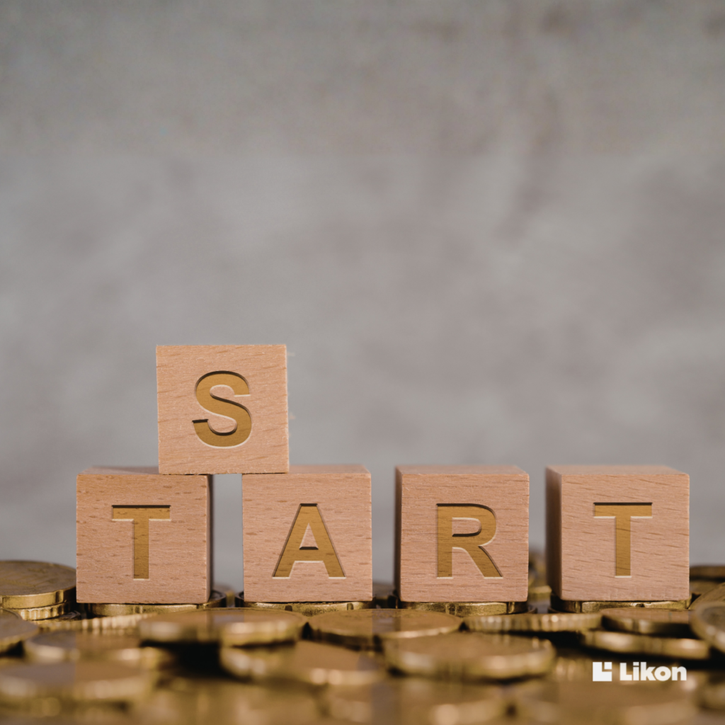 Drewniane kostki układające słowo „START” ustawione na monetach, symbolicznie przedstawiające początek planowania finansowego lub inwestycji.